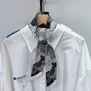 Detail of camellia flower pattern skinny scarf tied on a white long sleeve shirt pocket