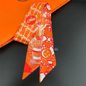 Close-up of orange floral silk twilly scarf with bird print on minimalist black background