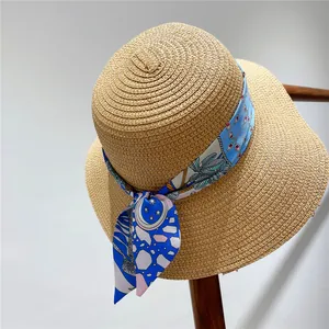 Detail of a wide brim straw hat featuring a blue floral silk ribbon with a bow decoration