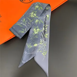 Close-up of a blue floral silk twilly scarf with France script next to an orange gift box