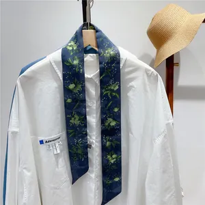 Detail of dark blue floral twilly scarf tied on a white shirt with a straw hat
