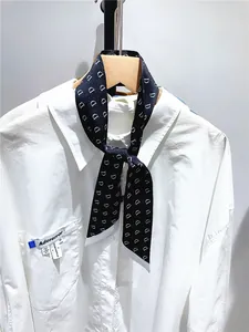 Macro detail of black silk twill ribbon scarf with white D letter print on shirt collar