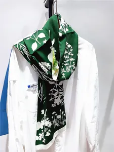 Détail d'un foulard en soie vert foncé avec motif floral noué sur un col blanc