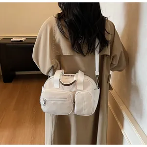 Sac bandoulière blanc multi-poches en nylon porté par un mannequin dans un salon