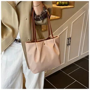Close-up of beige pleated tote bag with thin brown leather straps and metal snap button