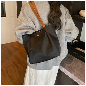 Detail view of large nylon tote bag with brown leather straps shown on a shoulder