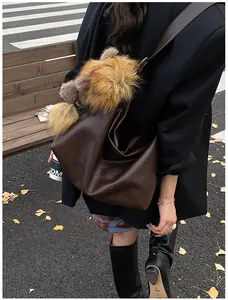Dettaglio di una borsa tote vintage marrone con ciondolo di peluche in una scena autunnale