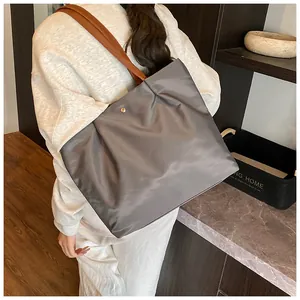 Detail of dark grey nylon tote bag with brown leather handles and golden metal snap button