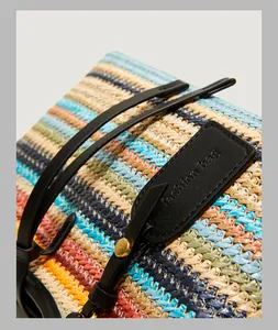 Detail of colorful woven fiber texture with a black leather tag and golden metal stud