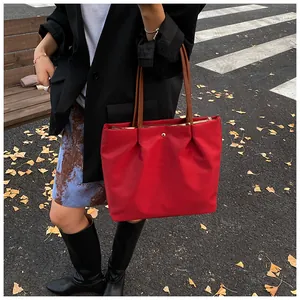 Outdoor street style shot of large red nylon tote bag with brown leather handles