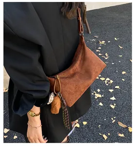 Close-up of brown suede shoulder bag with bear pendant and fringe tassel detail