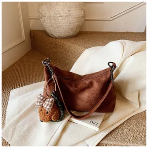 Macro detail of dark brown suede shoulder bag with a cute teddy bear plush charm