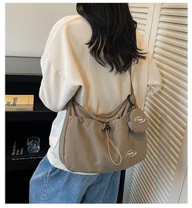 Detail of a large brown nylon crossbody bag with an adjustable strap and small round pouch