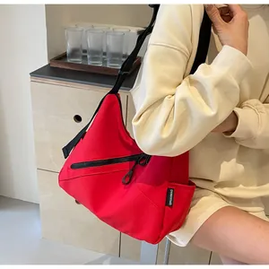Close-up of a large red canvas hobo bag with wide black strap and zipper detail