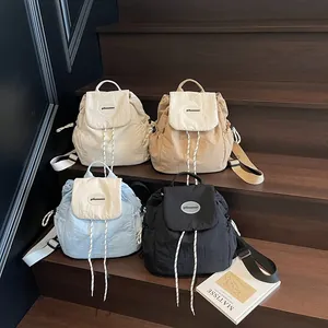Zaini minimalisti in nylon nei colori beige, kaki, blu e nero su gradini in legno