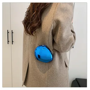 Detail of metallic blue pebble-shaped mini bag with gold chain on a brown blazer