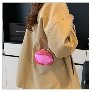 Detail of a bright pink oval acrylic crossbody bag with a gold metal chain strap on a model