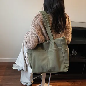 Olive green corduroy tote bag with multi-pocket design shown being worn by a model