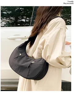 Outdoor shot of a black crescent nylon crossbody bag featuring wide straps and metal zippers
