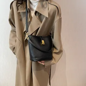Retro black bucket bag with gold lock and textured leather worn with trench coat