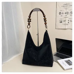 Detail einer schwarzen Hobo-Tasche aus Wildleder mit braunen Holzperlen und Metallringgurt
