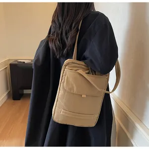 Detail of khaki nylon shoulder bag with vertical quilting and front pocket on model