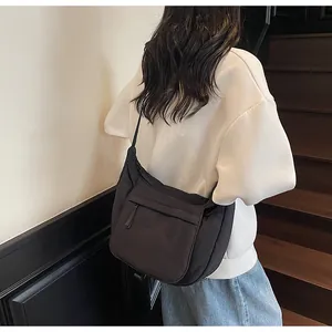 Side view of a large black nylon crossbody bag worn with a casual white sweatshirt