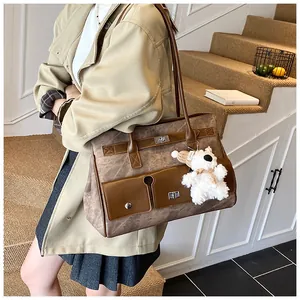 Detail of a brown leather tote bag with metal turn-lock pockets and a plush bear charm