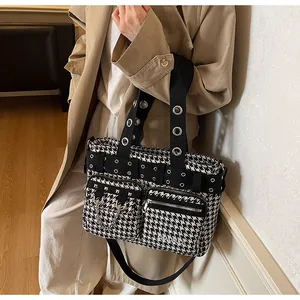 Detail of houndstooth tote bag featuring metal eyelets, chain decor, and wide woven strap
