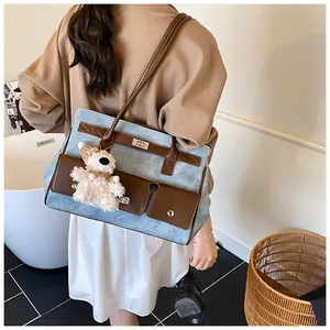 Detail of blue denim tote bag featuring brown leather trim and cute plush bear charm