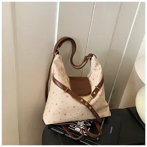Close-up of beige canvas shoulder bag featuring pink polka dots and brown leather details