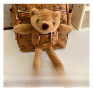 Detail showing a plush brown bear keychain with a metal logo on a leather backpack