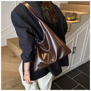 Detail of dark coffee hobo bag in glossy oil wax leather worn with a navy blazer