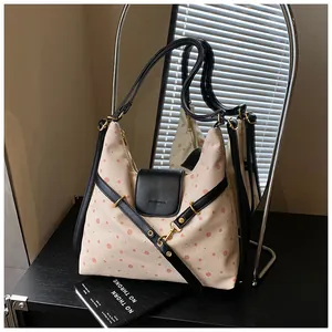 Detail of beige polka dot canvas bag featuring black leather trim and gold metal hardware