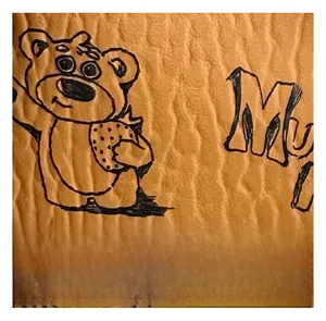 Macro detail of brown textured material featuring hand-drawn cartoon bear and letters