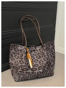 Detail of leopard print tote bag with brown leather handles and vintage charm pendant