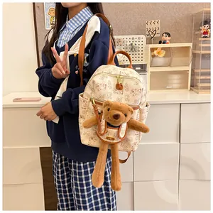 Detail of cream backpack with cartoon bear prints and a long-legged plush toy in front pocket
