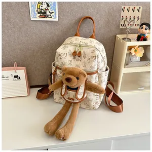 Detailed view of cream-colored backpack with plush bear and textured faux leather finish