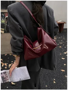 Detail of burgundy patent leather hobo bag featuring a gold crescent hardware clasp