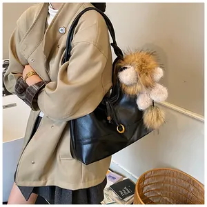 Detail of black leather tote bag featuring a cute plush lion pendant and gold hardware