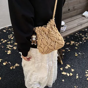 Handmade beige macrame bucket bag with doll charm on a park bench background