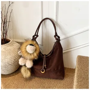 Detail of brown faux suede hobo bag featuring a golden ring and a cute lion plush charm