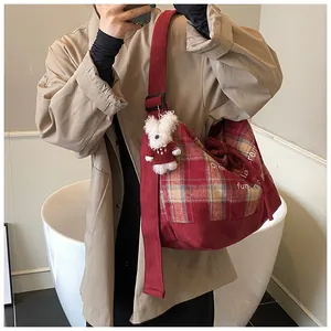 Detail of red plaid tote bag with plush bunny charm and white text print on strap