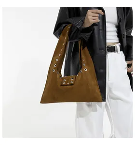 Detail of caramel suede shoulder bag with silver rivet eyelets worn with a black jacket