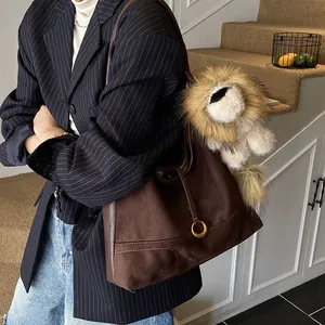 Brown faux suede tote bag with lion plush charm worn by model in a casual indoor setting