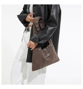 Close-up of brown suede shoulder bag with silver rivet grommets on a model