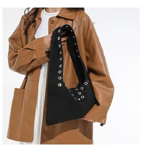 Detail of black suede shoulder bag with metallic silver rivets on model in brown leather