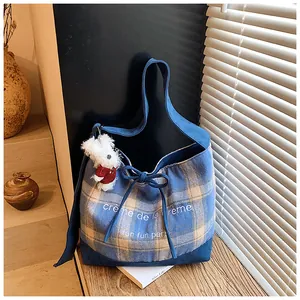 Detail of blue plaid tote bag with bow tie, text embroidery, and plush puppy charm