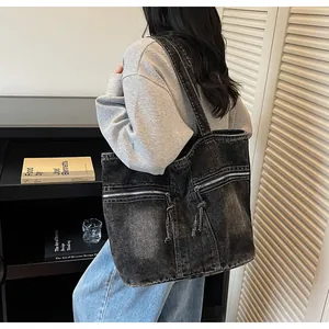 Detail of grey washed denim tote bag with dual metal zipper pockets and shoulder strap