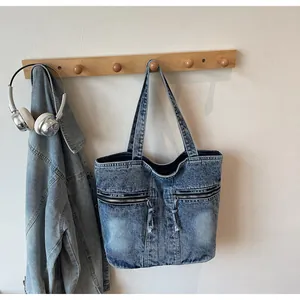 Detail of blue denim tote bag with dual metal zipper pockets and washed fabric texture